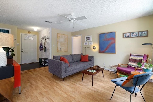 living area featuring light wood-style floors, a textured ceiling, a ceiling fan, baseboards, and visible vents