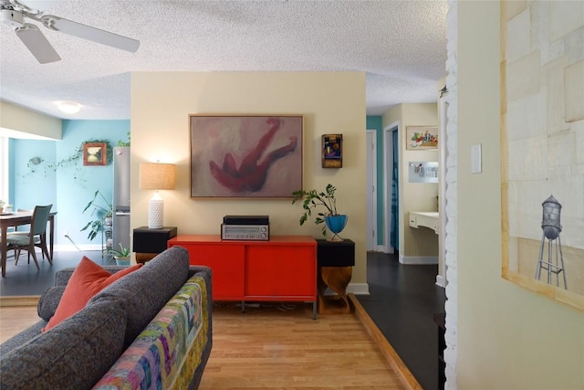 living room with a textured ceiling, ceiling fan, and wood finished floors