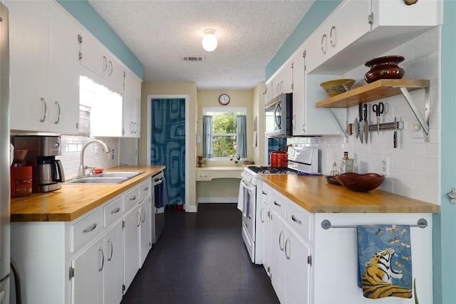 kitchen featuring a sink, wood counters, a textured ceiling, stainless steel appliances, and decorative backsplash