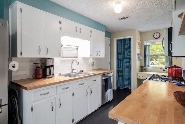 kitchen with a sink, wooden counters, stainless steel appliances, tasteful backsplash, and visible vents