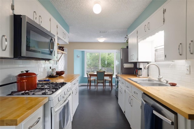 kitchen with appliances with stainless steel finishes, a sink, a textured ceiling, decorative backsplash, and visible vents