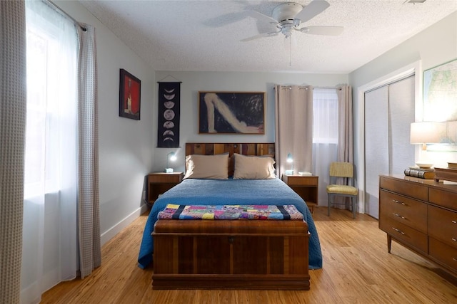 bedroom with a closet, baseboards, a textured ceiling, a ceiling fan, and light wood finished floors