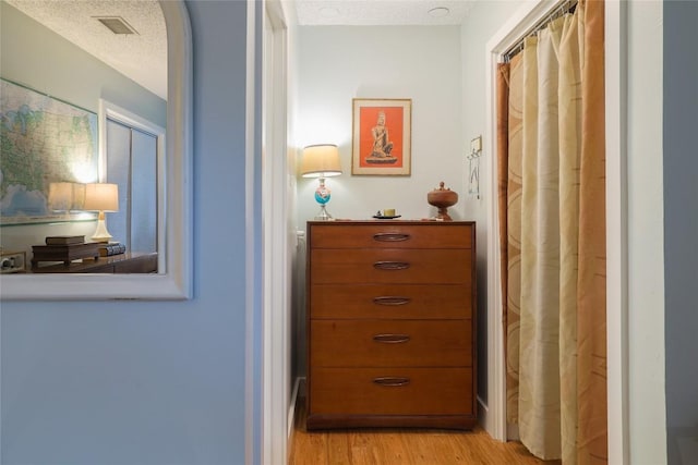 hallway with light wood-type flooring, a textured ceiling, and visible vents