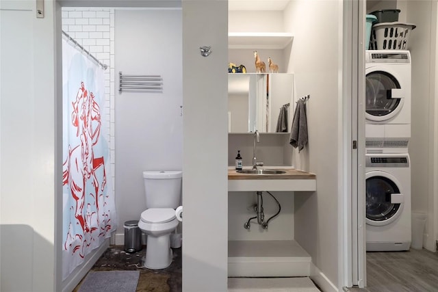 full bathroom with a sink, toilet, baseboards, stacked washer / dryer, and wood finished floors