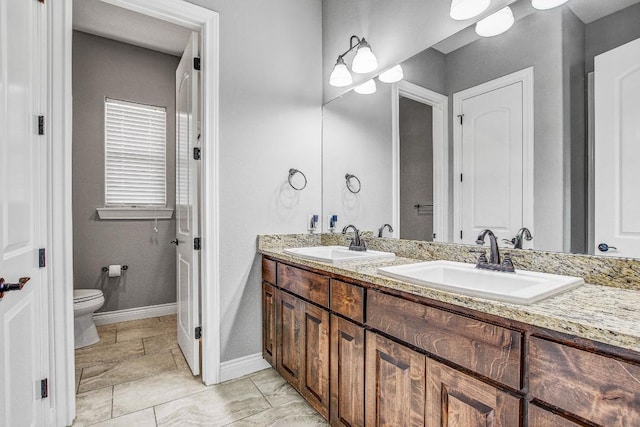 bathroom with double vanity, toilet, baseboards, and a sink