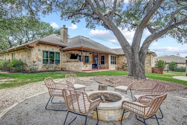 rear view of property with a chimney, a patio area, fence, a fire pit, and stone siding