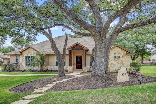 view of front of house featuring a front lawn, stucco siding, stone siding, and fence