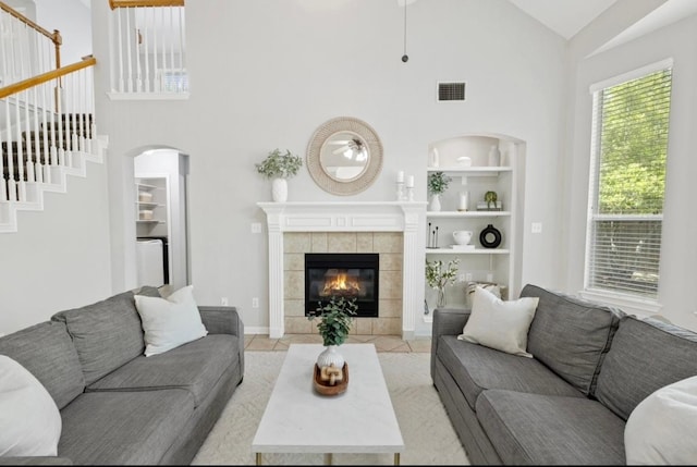 tiled living area featuring high vaulted ceiling, built in features, a tiled fireplace, stairs, and visible vents