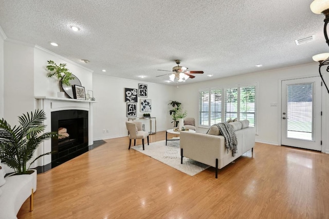 living area with crown molding, light wood finished floors, a fireplace, a textured ceiling, and visible vents