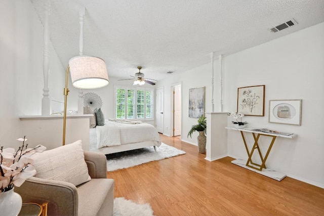bedroom with baseboards, a textured ceiling, visible vents, and wood finished floors
