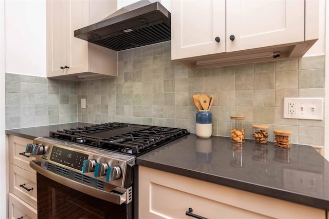 kitchen with wall chimney range hood, stainless steel range with gas stovetop, dark countertops, tasteful backsplash, and white cabinets