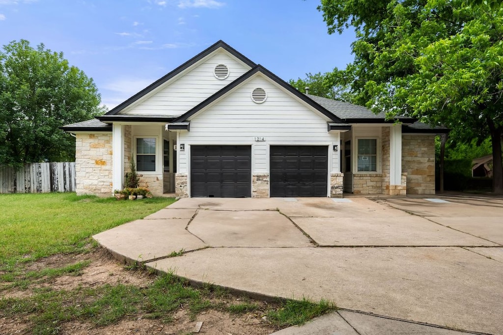 view of front facade with fence, a front lawn, stone siding, a garage, and driveway