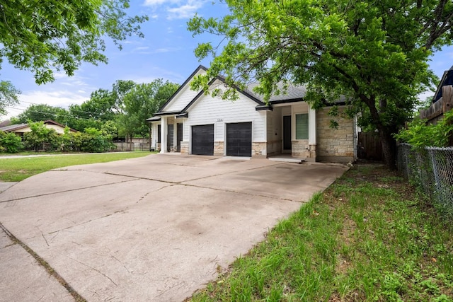 view of home's exterior with driveway, a lawn, fence, an attached garage, and stone siding