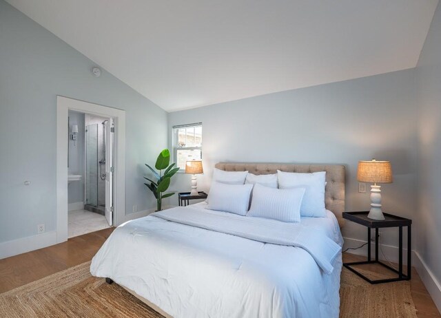 bedroom featuring wood finished floors, baseboards, ensuite bathroom, and lofted ceiling