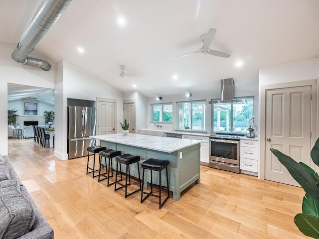 kitchen with stainless steel appliances, a ceiling fan, a kitchen bar, a kitchen island, and vaulted ceiling