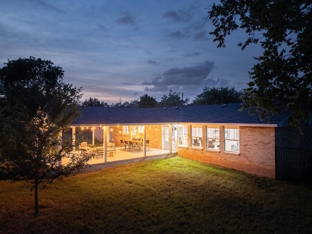 5203 Branding Chase St, Austin, TX 78727 - back of property at dusk with a lawn, brick siding, and a patio