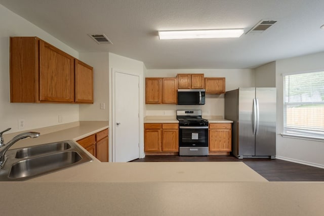 292 Dandelion Loop, Kyle, TX 78640 - kitchen featuring appliances with stainless steel finishes, a sink, brown cabinetry, dark wood-style floors, and light countertops
