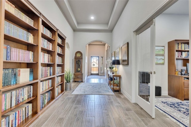 foyer entrance with arched walkways, baseboards, light wood-type flooring, and a towering ceiling