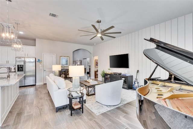 living area featuring arched walkways, ceiling fan with notable chandelier, light wood-type flooring, and visible vents