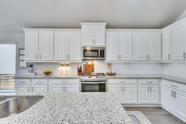 kitchen featuring appliances with stainless steel finishes, tasteful backsplash, light wood-type flooring, light stone counters, and white cabinetry