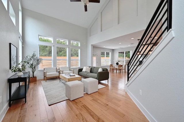 living area featuring ceiling fan, light wood finished floors, stairs, and a high ceiling