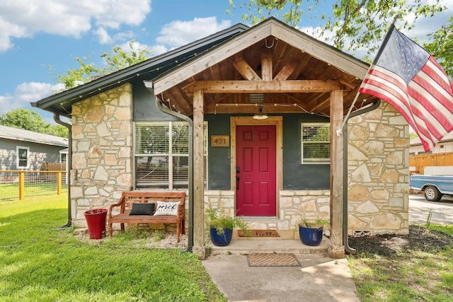 property entrance with a lawn, fence, and stone siding