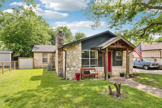 bungalow-style home featuring a front lawn, fence, stone siding, a chimney, and central AC unit