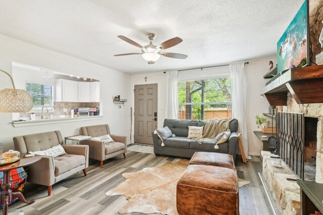 living area with plenty of natural light, ceiling fan, a fireplace, and light wood-type flooring