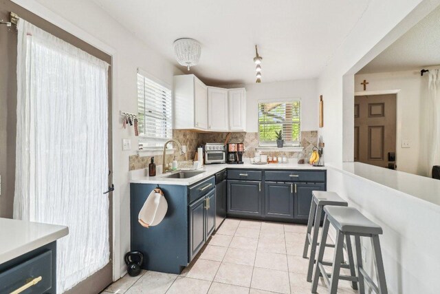 kitchen with a sink, decorative backsplash, light tile patterned flooring, and light countertops