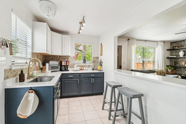 kitchen with light tile patterned flooring, light countertops, white cabinets, a sink, and backsplash