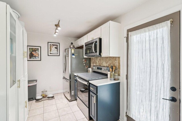 kitchen with appliances with stainless steel finishes, tasteful backsplash, light countertops, white cabinets, and light tile patterned flooring