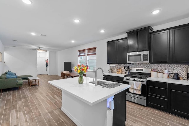 kitchen featuring open floor plan, dark cabinetry, a sink, light wood-style flooring, and stainless steel appliances