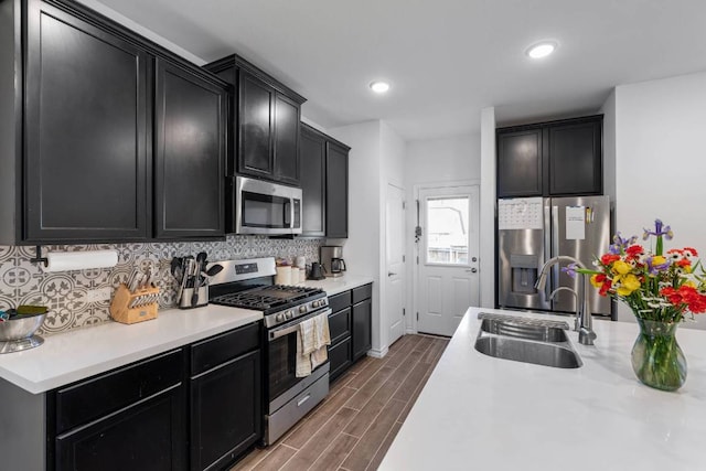 kitchen with light countertops, tasteful backsplash, dark cabinets, a sink, and appliances with stainless steel finishes