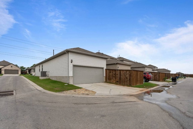 view of home's exterior with driveway, a residential view, a garage, fence, and cooling unit