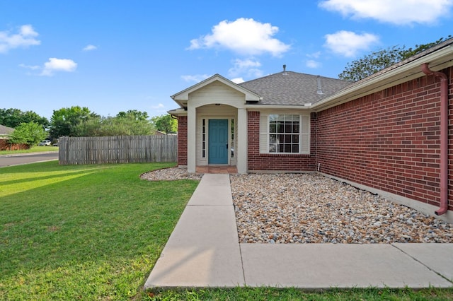 view of front of home with brick siding, fence, a shingled roof, and a front yard