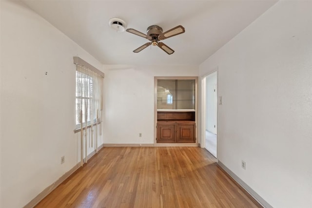 empty room featuring baseboards, a ceiling fan, and light wood-style flooring