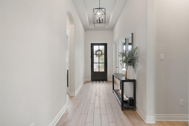 doorway with an inviting chandelier, arched walkways, light wood finished floors, and baseboards