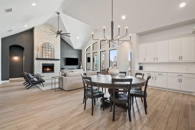dining area featuring a fireplace, visible vents, light wood finished floors, and ceiling fan with notable chandelier