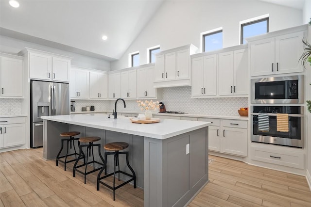 kitchen featuring white cabinets, a breakfast bar, high vaulted ceiling, an island with sink, and stainless steel appliances