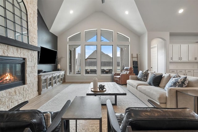 living area with a stone fireplace, light wood-style floors, baseboards, high vaulted ceiling, and recessed lighting