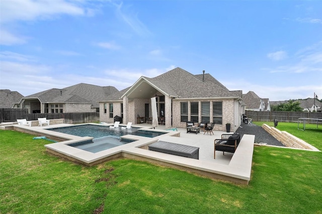 back of house with an in ground hot tub, a trampoline, a lawn, a patio area, and a fenced in pool
