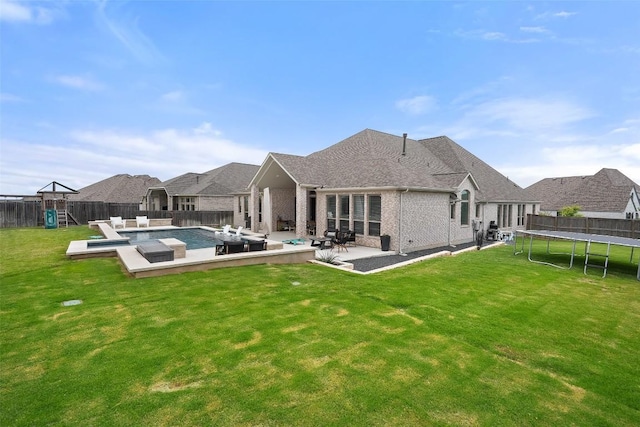 rear view of property with a fenced backyard, brick siding, a patio area, a lawn, and a trampoline