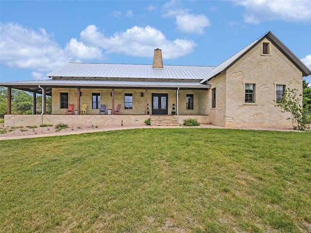 view of front of property with covered porch, a front yard, stucco siding, a chimney, and metal roof