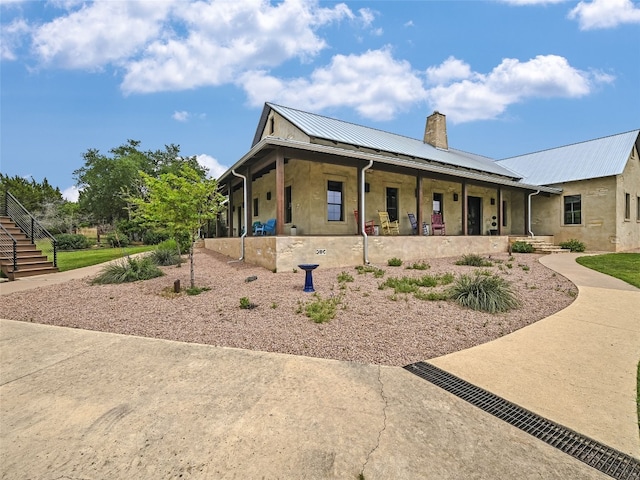 view of front facade with covered porch, a standing seam roof, metal roof, a chimney, and stairs
