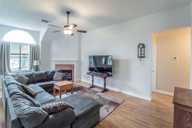 living area with visible vents, light wood-style floors, baseboards, a tile fireplace, and a ceiling fan