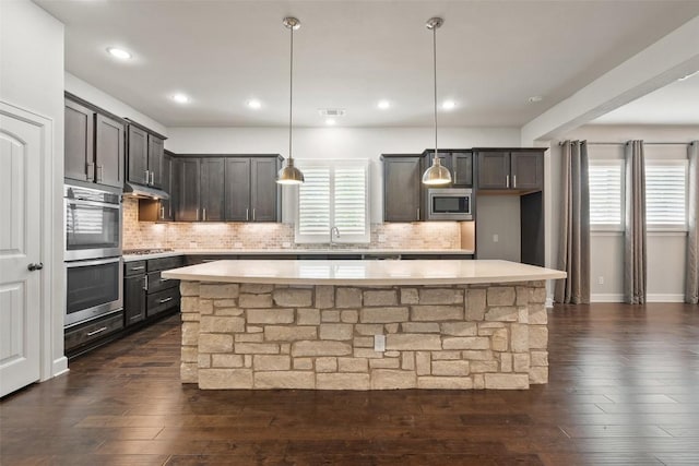 103 Lockhart Loop, Georgetown, TX 78628 - kitchen with stainless steel appliances, a center island, light countertops, dark wood-style flooring, and tasteful backsplash