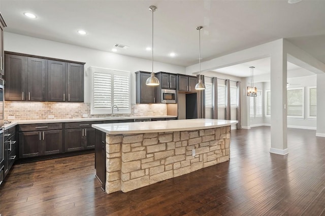 103 Lockhart Loop, Georgetown, TX 78628 - kitchen with stainless steel microwave, backsplash, dark brown cabinets, light countertops, and a center island