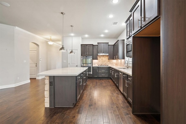 103 Lockhart Loop, Georgetown, TX 78628 - kitchen featuring stainless steel appliances, arched walkways, decorative backsplash, a kitchen island, and dark wood-style flooring