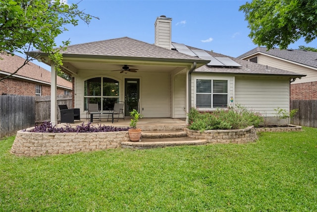 back of house featuring roof mounted solar panels, a fenced backyard, a patio area, a ceiling fan, and a yard