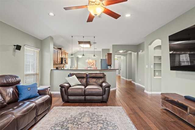 living area with arched walkways, ceiling fan, dark wood finished floors, and baseboards